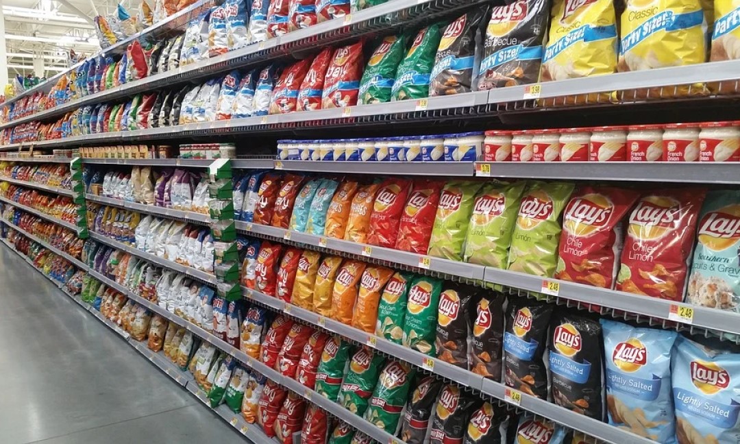 A store aisle with shelves full of packaged chips and other foodstuffs.
